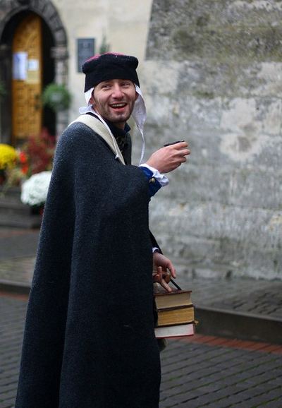 An actor in a beret with a cup and a stack of books, laughing
